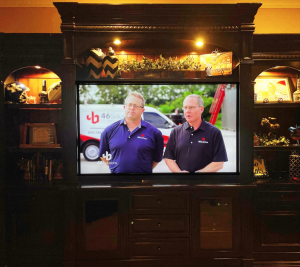 Large flat screen tv installed in an entertainment center set up with two members from the 46 Solutions team on the screen.