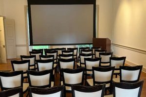 Conference room with a projector screen and chairs arranged for an audience.