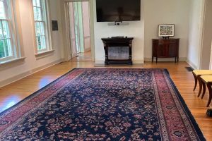 20240606_201107616_iOS Spacious room with a Persian rug, a mounted TV, and large windows providing natural light.