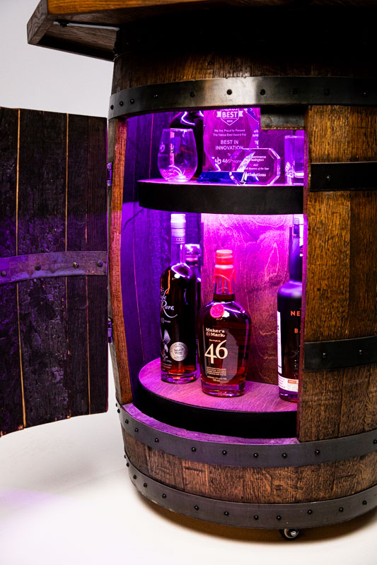 A detailed view of the bourbon barrel bar, showcasing various bottles, glasses, and decorative awards under blue lighting.
